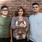 A loving family poses together outdoors against a brick wall.