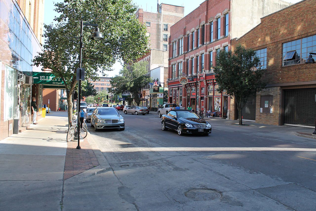La 4th Street del centro de Des Moines, Iowa, con comercios y vehículos — placas temporales cerca de ti